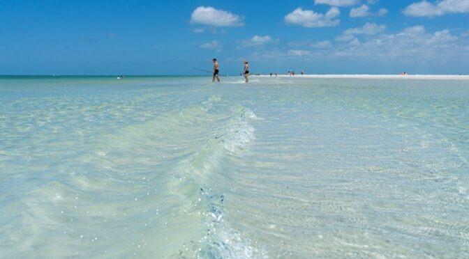 Clearwater Beach white sand shoreline with families enjoying calm Gulf waters, blue skies, and umbrellas along the coast near Tampa Bay