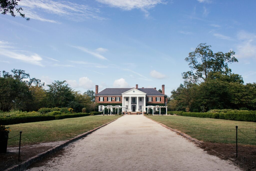 Symmetrical brick mansion with columns at end of long path and landscaped lawn