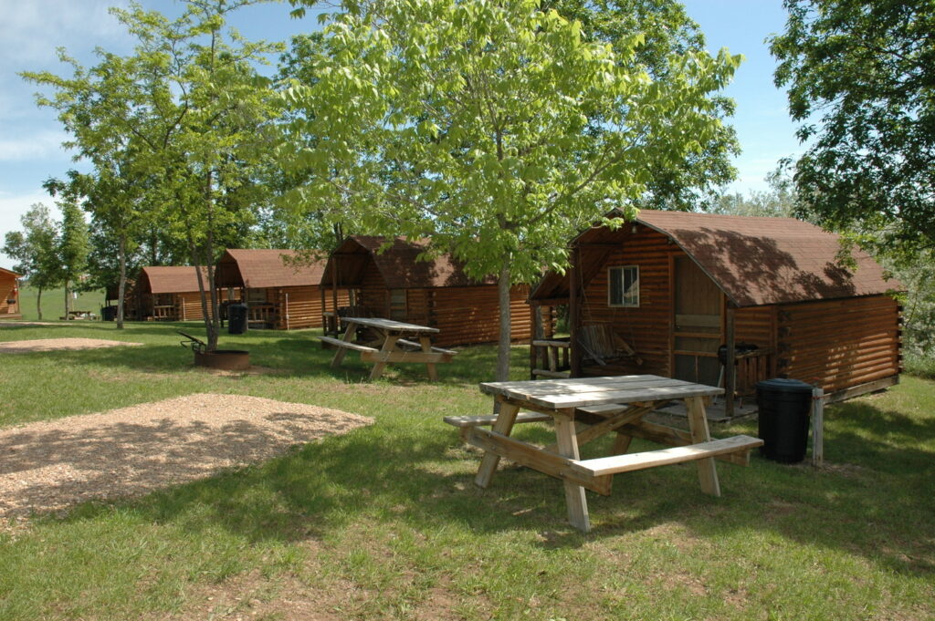 Row of wooden cabins with picnic tables and trees at campground