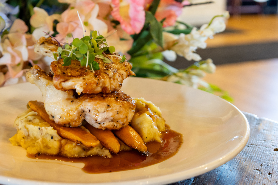 Grilled chicken served over mashed potatoes with vegetables and sauce