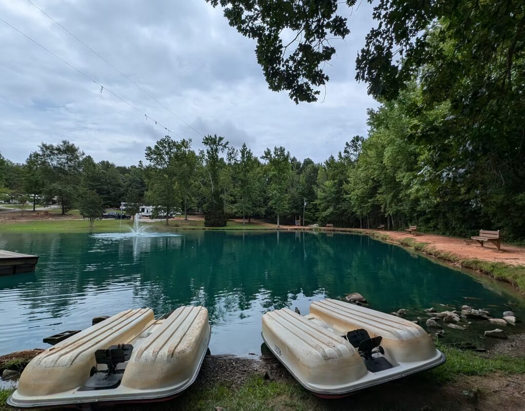 Paddle boats by calm campground pond with fountain and wooded surroundings