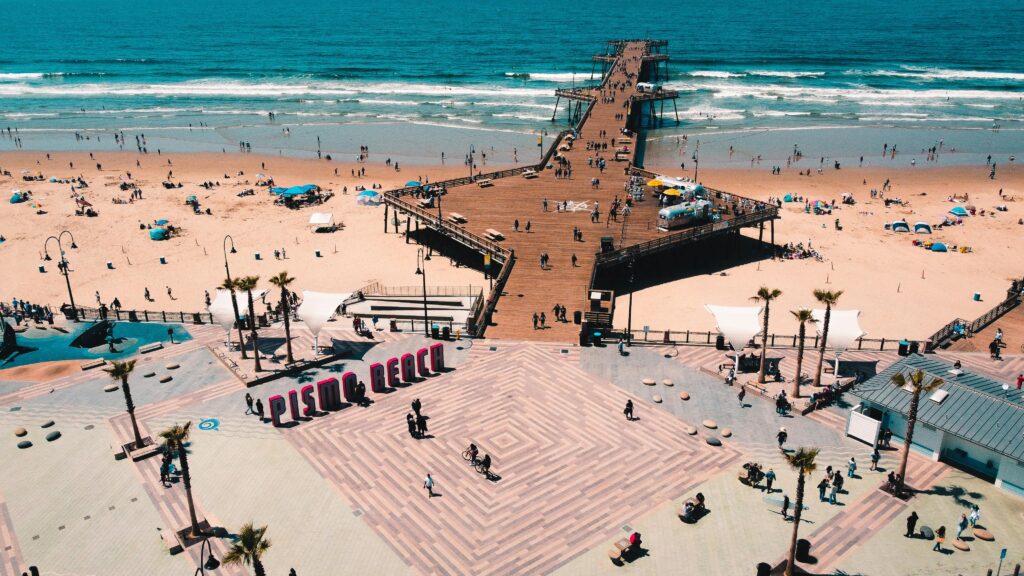 Aerial view of Pismo Beach pier, sandy shoreline, and beachfront boardwalk on sunny day