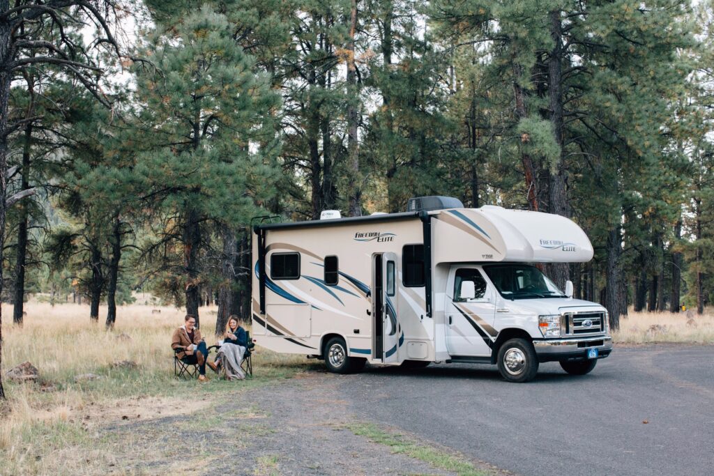 Couple relaxing beside motorhome during RV camping in wooded campground