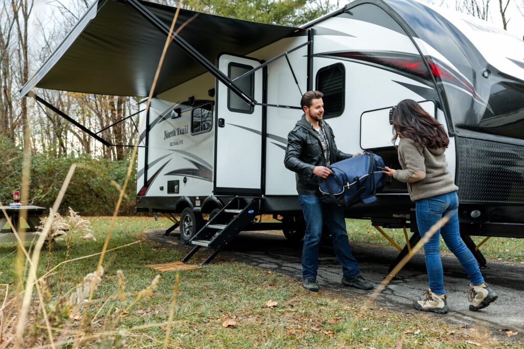 Couple unloading bags beside travel trailer during RV camping trip