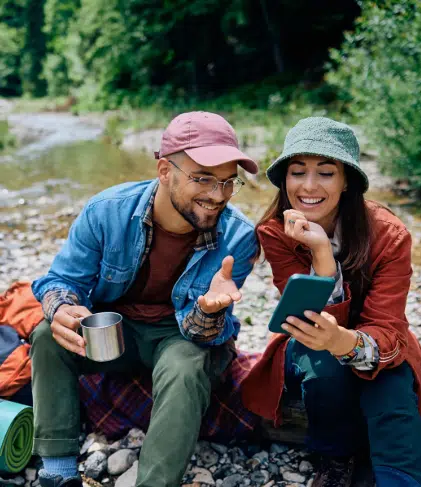 Two campers looking at a phone by a river