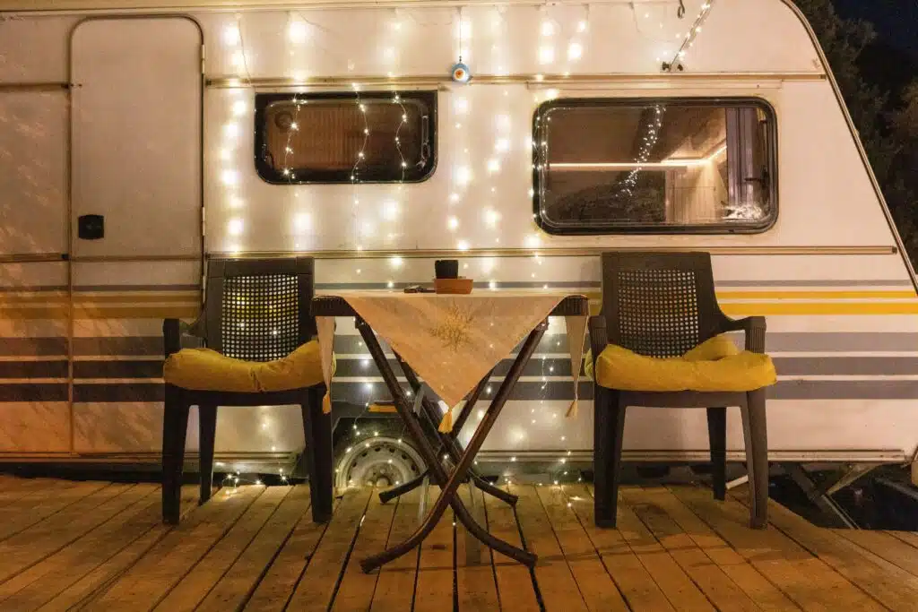 Cozy RV campsite setup with string lights, outdoor chairs, and a small table creating a warm evening camping atmosphere.